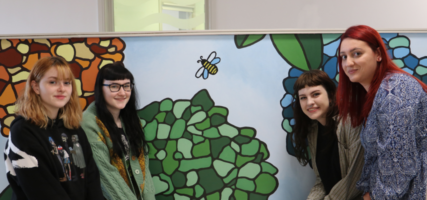 four students crouched in front of a mural painted at Bury Hospice