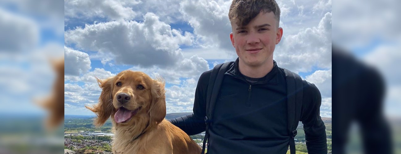 Former Bury College A-level student, Adam Kenzitt, sat on a hill with a dog