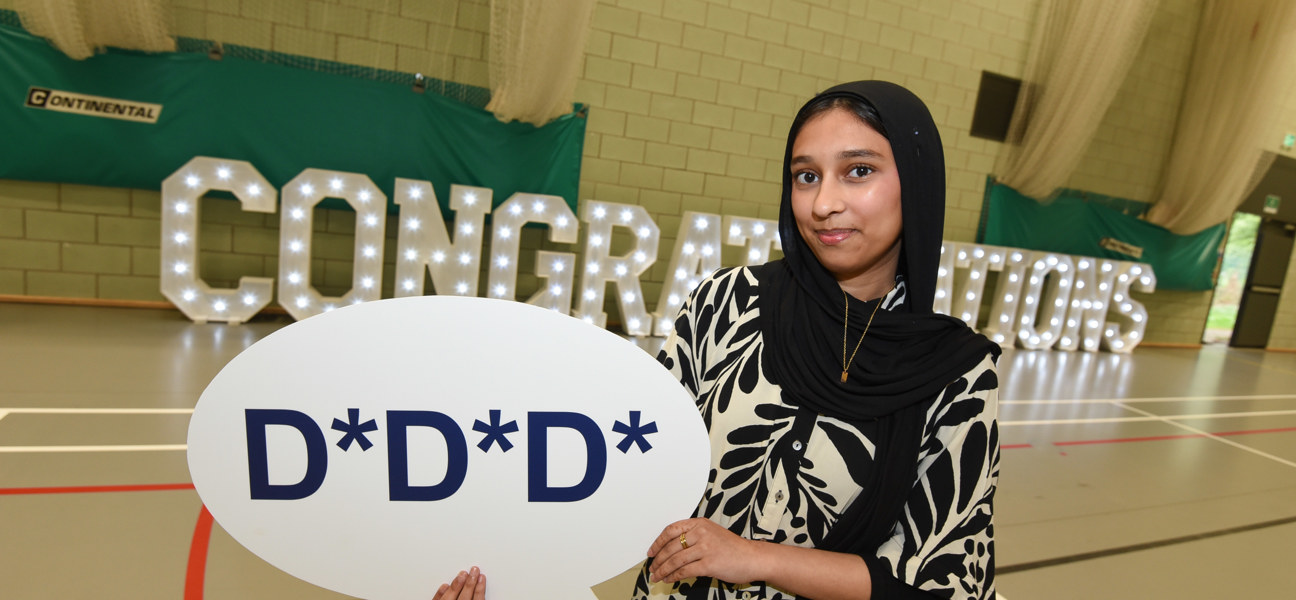 student stood holding up D* D* D* sign in front of congratulations letters