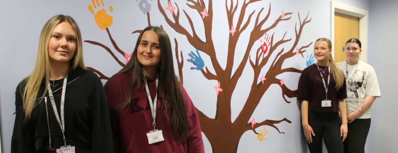 art students stood in front of tree mural