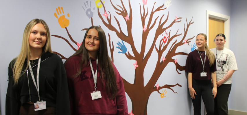 art students stood in front of tree mural