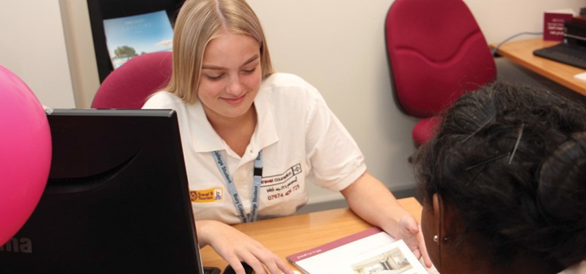  International Tourism Management HE student sat at a desk showing a travel brochure to another student 