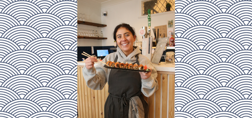 owner of codi's kitchen stood holding a plate of sushi