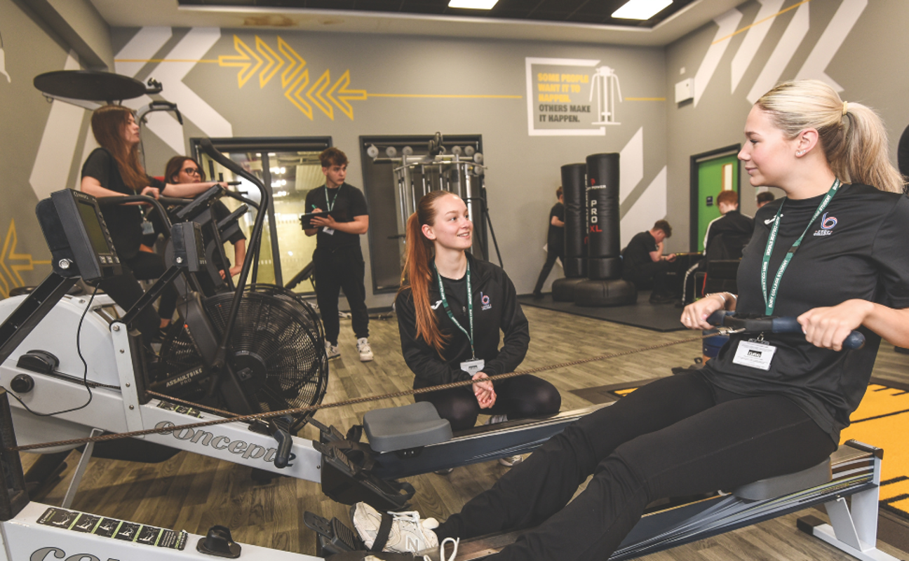 students in the gym with one on a rowing machine