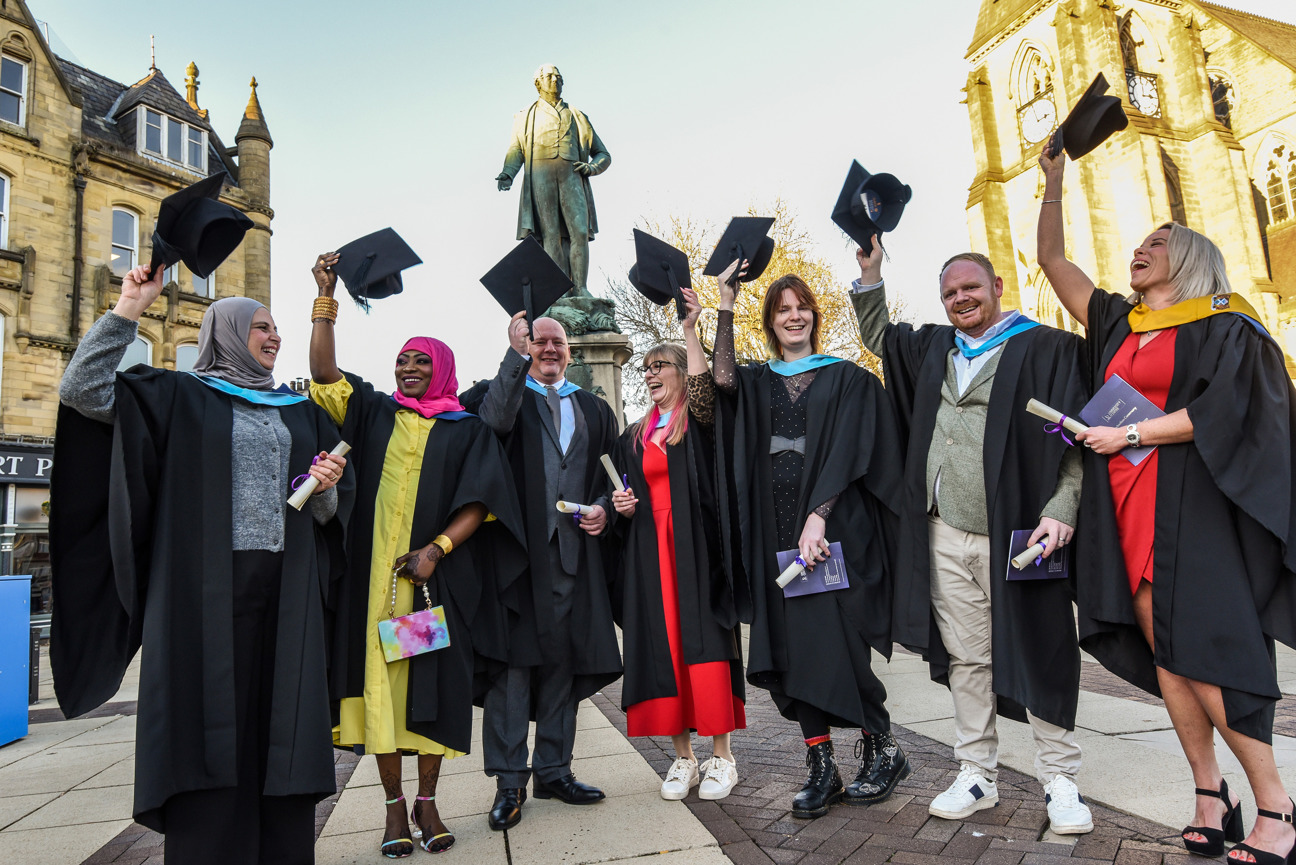 students stood in a row with their caps aloft on graduation day