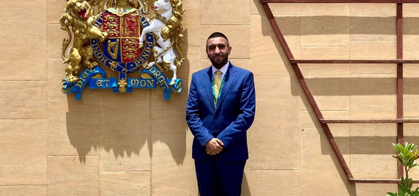 A former Bury College A-level student being awarded an MBE for his services to British Nationals overseas, in front of a crest