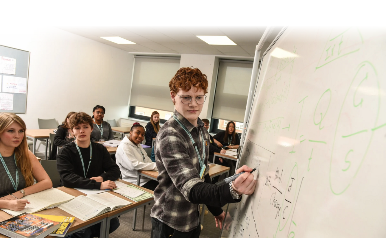 student writing on a whiteboard at the front of the class