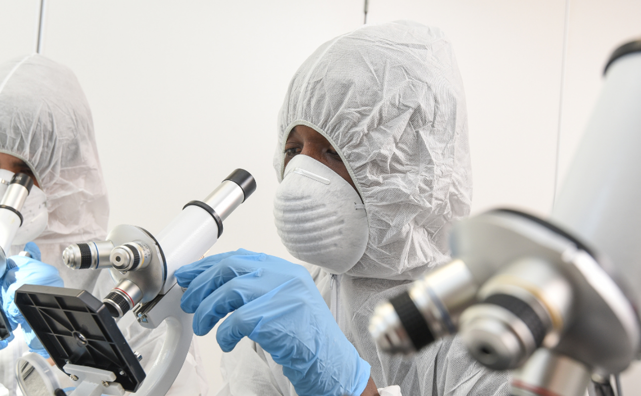 public services student in forensics outfit inspecting something with microscope