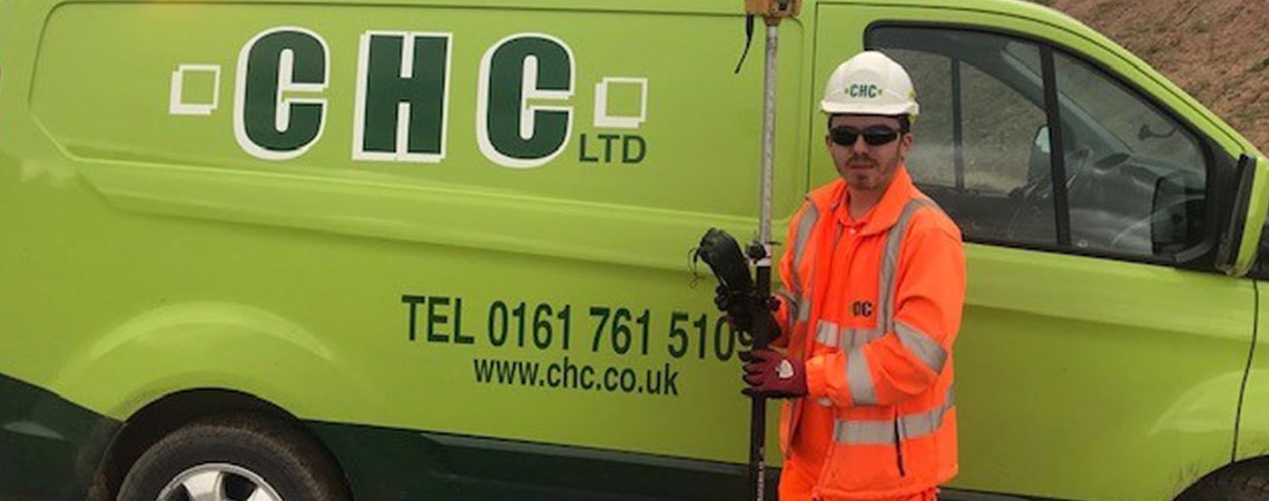 A Bury College student, wearing high visibility workwear, stood infront of a Cheetham Hill Construction van