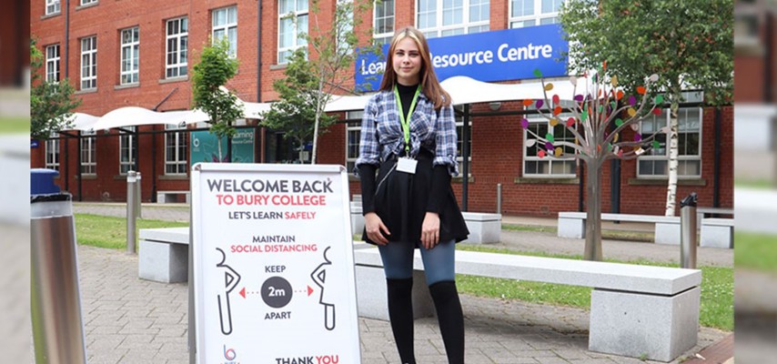 Student stood in front of the Learning Resource Centre next to a sign explaining social distancing