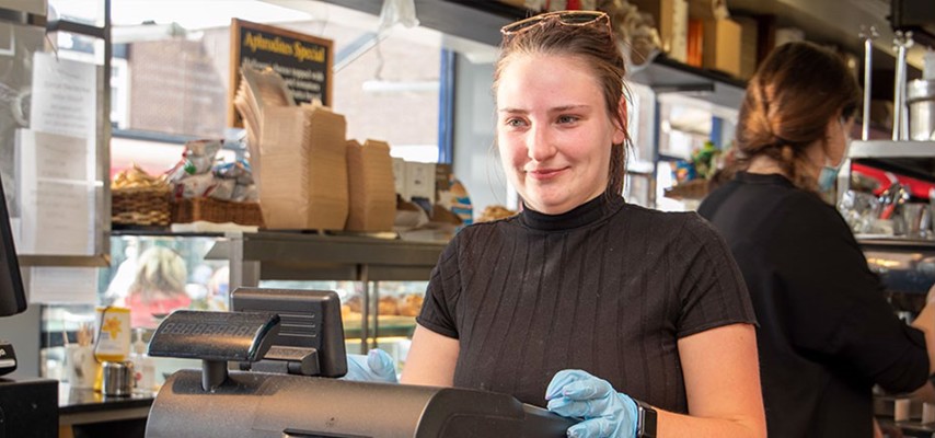 A female Bury College student stood behind a till dressed in black