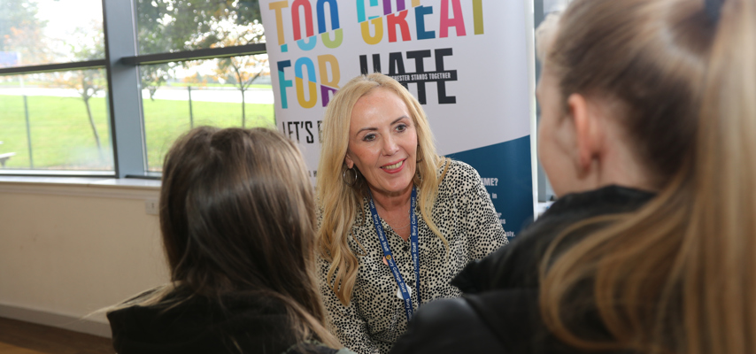 woman stood speaking with two students at a hate crime awareness stand